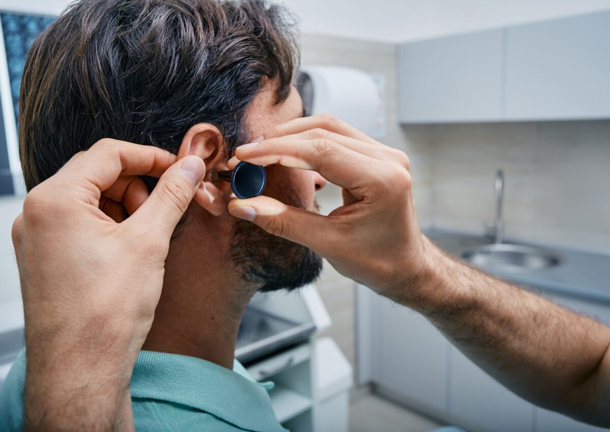 ENT doing professional examination of male patient's ear in his office at medical clinic. Ear check-up, close-up