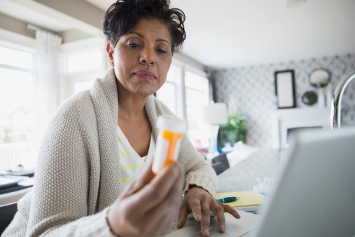 Woman reading prescription bottle label at laptop
