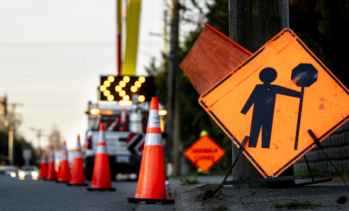 Lane closure on a busy road due to maintenance signs detour traffic temporary street work orange lighted arrow, barrels, and cones.