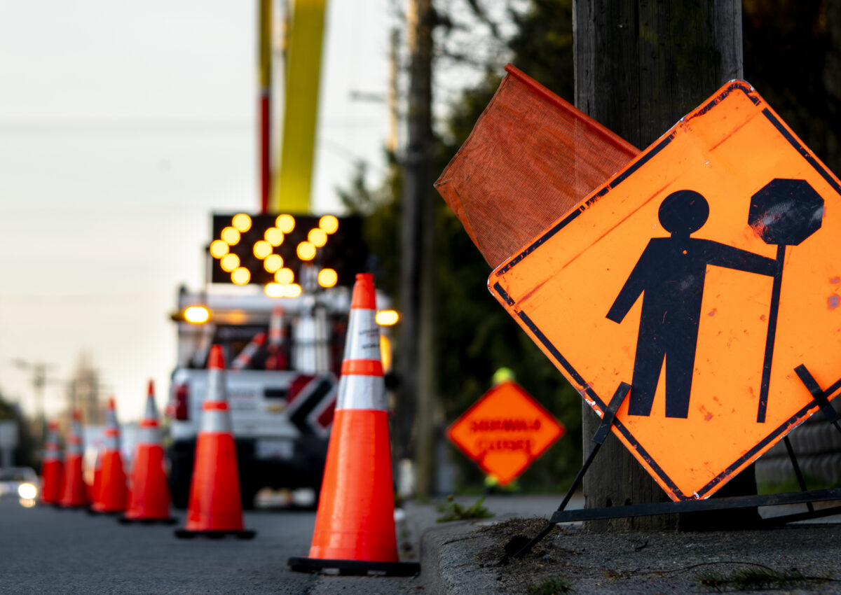 Lane closure on a busy road due to maintenance signs detour traffic temporary street work orange lighted arrow, barrels, and cones.